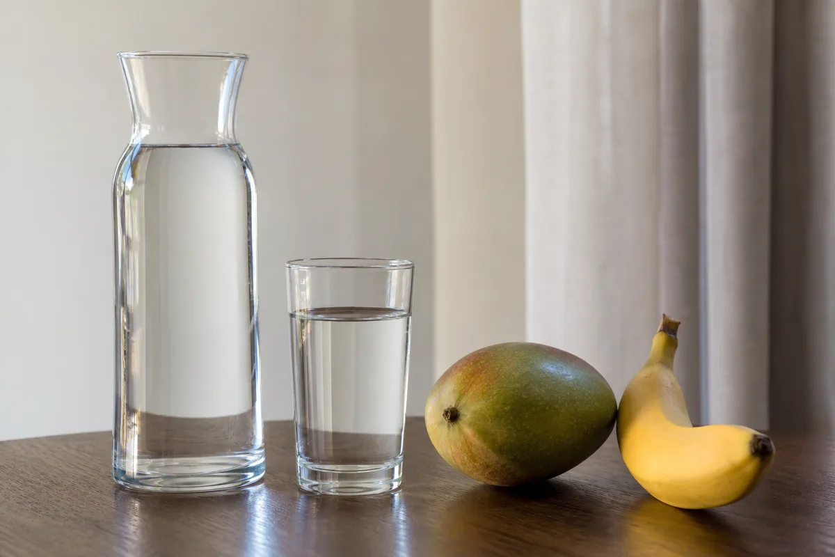 Carafe en verre lisse et fruits entiers sur une table de chambre d’hôtel baignée de lumière naturelle